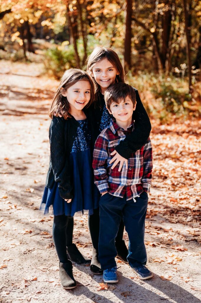 Photo of three kids in the woods during fall