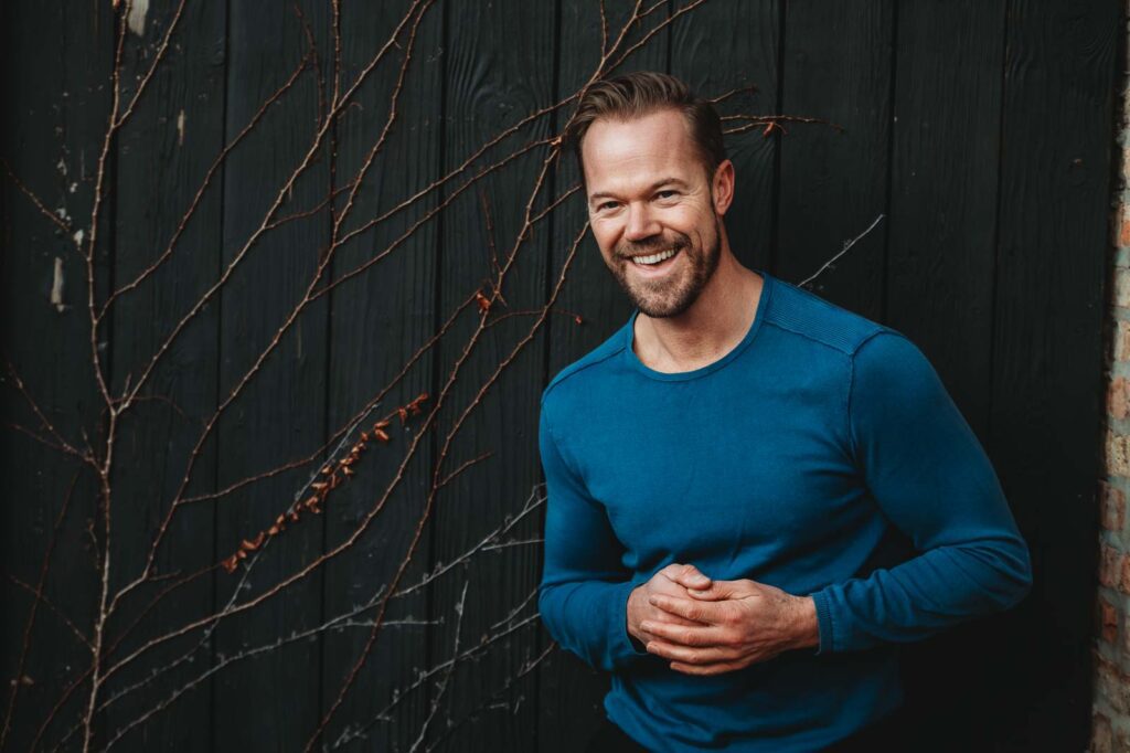 man smiling against a brick wall